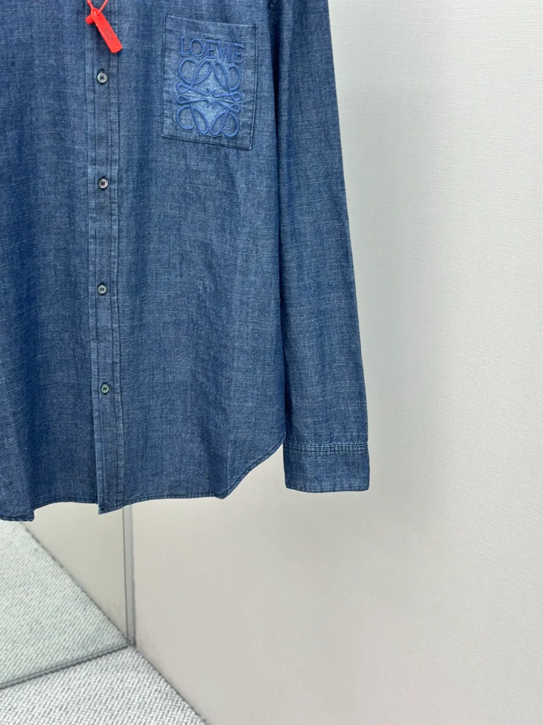 P430 Loewe Anagram Gradient Embroidered Pocket Shirt Made of custom-made high-quality cotton chambray fabric, with a unique washed gradient blue as the main tone, from dark to light and from thick to light. The chest patch pocket is decorated with Loewe Anagram embroidery as its soul, engraved with LOEWE-style casual elegance, and the natural and smooth lines show the casualness.  Imported embroidery machines are used, and advanced computer control systems and precision mechanical components are used to realize Loewe embroidery operations.  The gradient dynamic spray dyeing process uses specialized spray dyeing equipment to accurately spray dye onto the surface of the fabric in the form of mist (by accurately controlling the different dimensions of the spray of the spray dyeing equipment, combined with the movement speed and direction during the dyeing process) to present a smooth and natural transition effect of color. The butterfly rhyme pinch pleating body dart technology is inspired by the beautiful shape of butterflies, and uses precise pinch pleating techniques to create a flexible pleat effect like butterfly wings on the garment, making the garment fit more closely to the body.  size:44.46.48.50